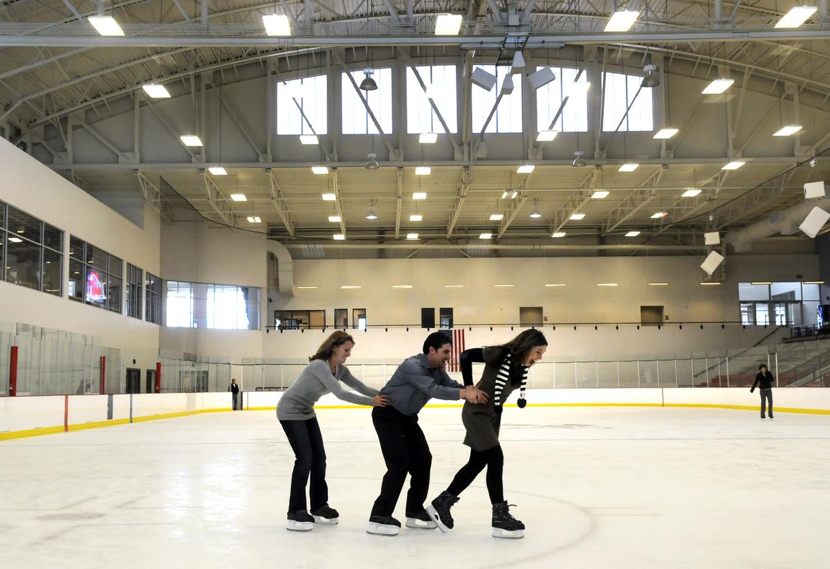three people skate in train formation on the ice rink